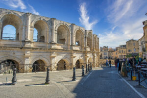 Außenansicht des Amphitheaters von Arles mit Passanten und Straßencafé in der Altstadt.