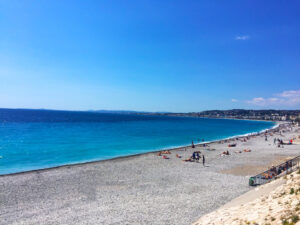 Kiesstrand an der Baie des Anges in Nizza mit Badegästen und Blick entlang der Küste