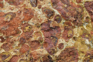 Nahaufnahme von rötlichem Bauxitgestein mit gelben und braunen Mineralstrukturen