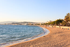 Sandstrand an der Croisette in Cannes bei warmem Abendlicht mit Palmenpromenade und Blick über die Bucht