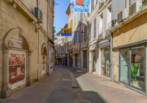 Schmale Altstadtgasse in Carpentras mit kleinen Geschäften und bunt bemalten Bannern