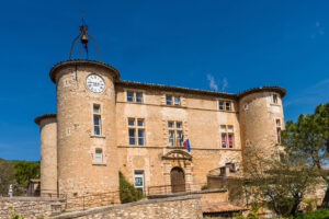 Frontansicht des Château de Rustrel mit Uhrturm und den Fahnen des Rathauses