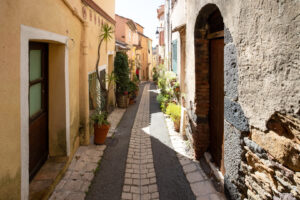 Sonnige Altstadtgasse in Cogolin mit ockerfarbenen Häusern und Pflanzen vor den Türen