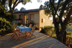 Ferienhaus in der Provence mit gedecktem Terrassentisch unter Bäumen im Abendlicht.