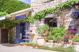 Blumengeschmücktes Steinhaus mit blauen Fensterläden im Dorfkern von Gourdon
