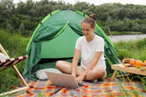 Frau nutzt einen Laptop neben einem Zelt beim Camping