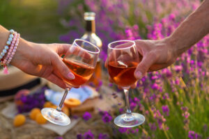 Zwei Gläser Roséwein beim Anstoßen zwischen blühenden Lavendelfeldern.