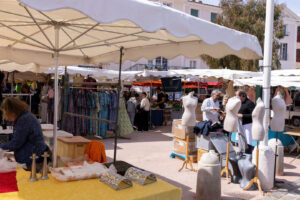 Markt in Port Grimaud mit Ständen, Kleidung und Besuchern unter weißen Sonnenschirmen
