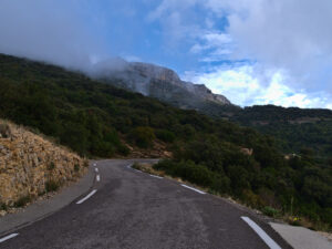 Kurvige Bergstraße im Massif de la Sainte-Baume mit bewaldeten Hängen, Kalkfelsen und tief hängenden Wolken
