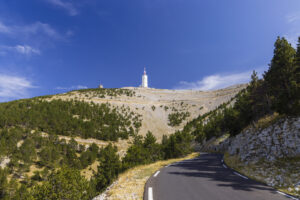 Straße zum Mont Ventoux mit Blick auf den Gipfel‑Sendeturm, karge Hänge und Pinienwald