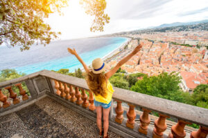 Frau mit Hut blickt von einem Aussichtspunkt auf Nizza und die Baie des Anges an der Côte d’Azur.
