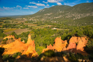 Ockerfelsen des Colorado Provençal vor Feldern und bewaldeten Höhen bei Rustrel