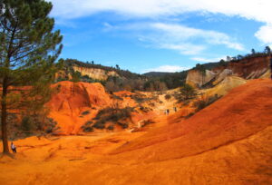 Orangefarbene Ockerhügel mit Wanderern und hellen Abbauwänden im Colorado Provençal bei Rustrel