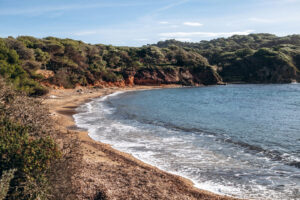 Plage du Langoustier auf Porquerolles mit ruhiger Bucht, roter Felsküste und Pinienwald