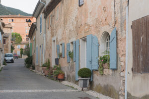 Schmale Gasse in Rustrel mit alten Steinhäusern, blauen Fensterläden und Blumen
