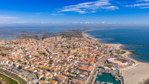 Luftaufnahme von Saintes-Maries-de-la-Mer mit Ortszentrum, Arena, Hafen, Strand und Lagunen der Camargue