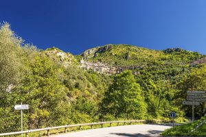 Straße nach Saorge mit Blick auf das Bergdorf zwischen grünen Hängen im Roya-Tal