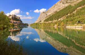 Blick über die Durance auf Sisteron mit Zitadelle, Felswänden und Spiegelung im Wasser