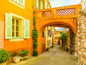 Schmale Altstadtgasse in Villefranche-sur-Mer mit orangefarbenen Fassaden, grünen Fensterläden und Steinmauer