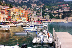 Hafen von Villefranche-sur-Mer mit Booten, bunten Häusern und Blick auf die Hügel der Côte d’Azur