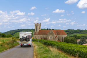 Wohnmobil fährt durch Weinberge in Südfrankreich mit kleiner Dorfkirche im Hintergrund.